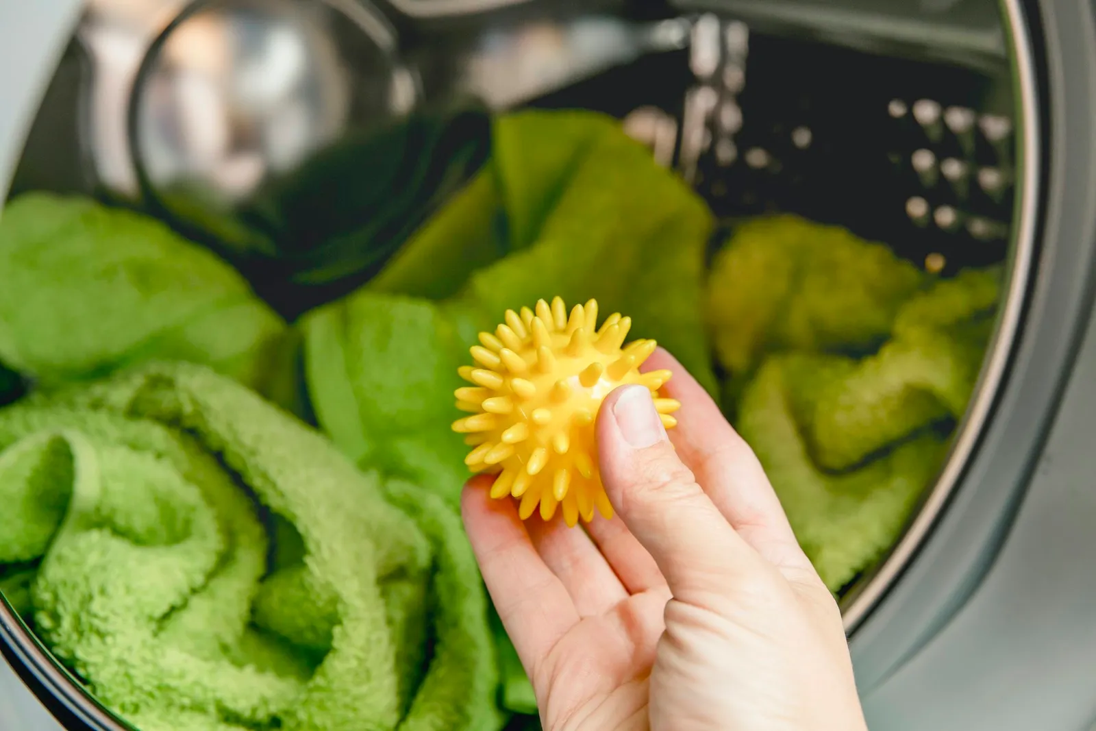 Using pvc dryer balls is natural alternative to both dryer sheets and liquid fabric softener, balls help prevent laundry from clumping in the dryer. Woman hand put in a yellow spiky dryer ball.