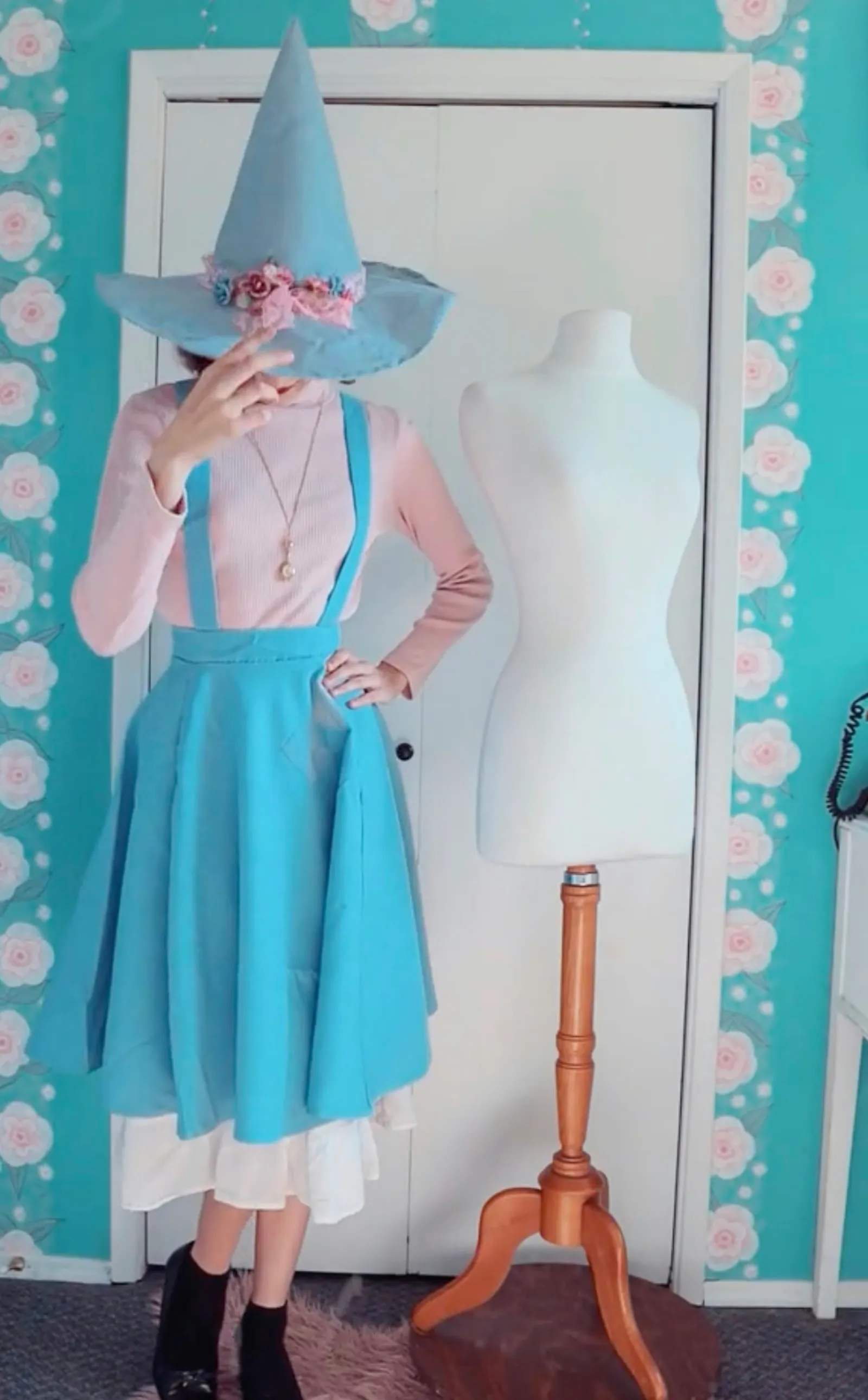Woman wearing a witch costume made with light blue and pastel pink fabric, including an embellished blue witch hat