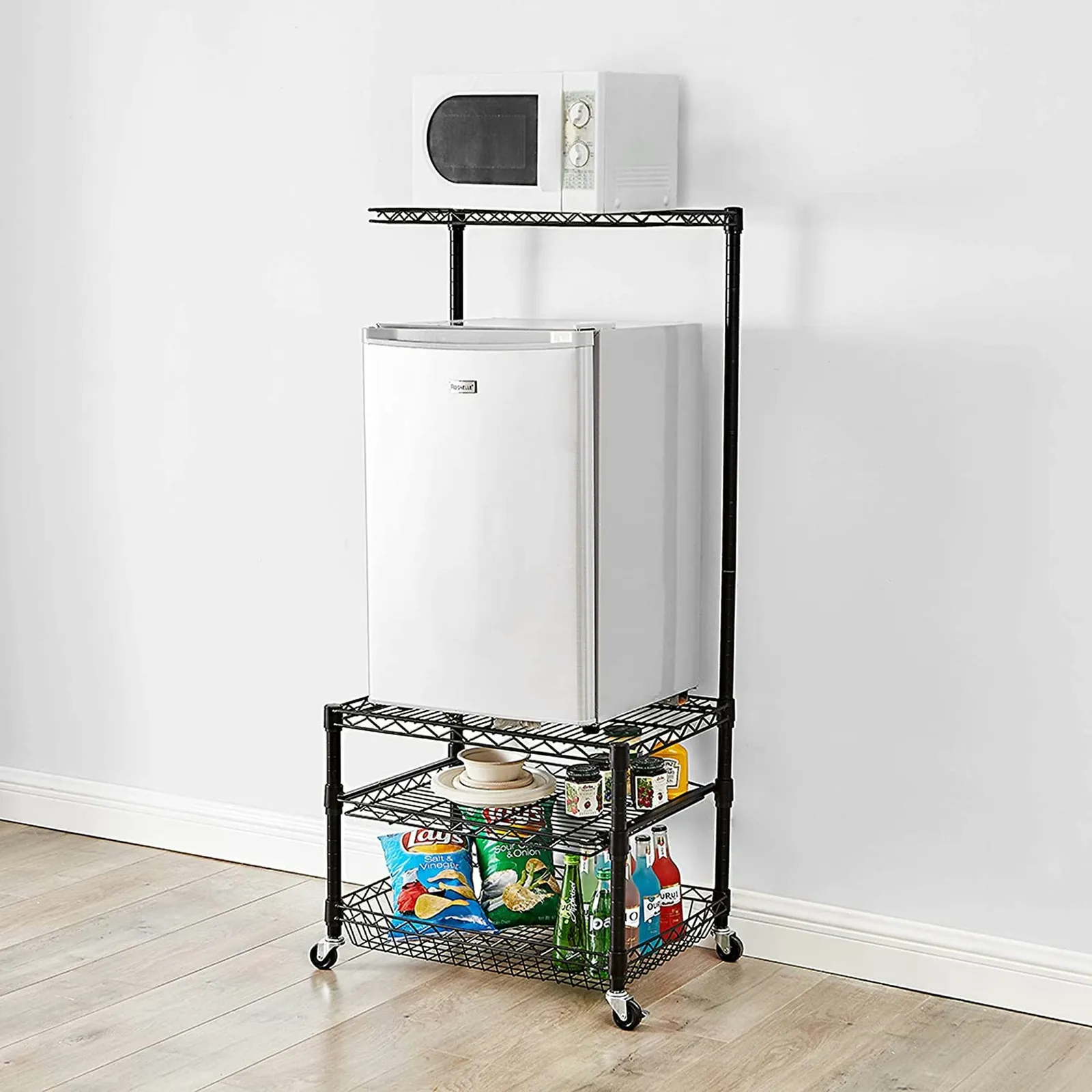 A rolling shelving unit with four shelves and cator wheels. A microwave sits on top and a mini fridge is on the second shelf.
