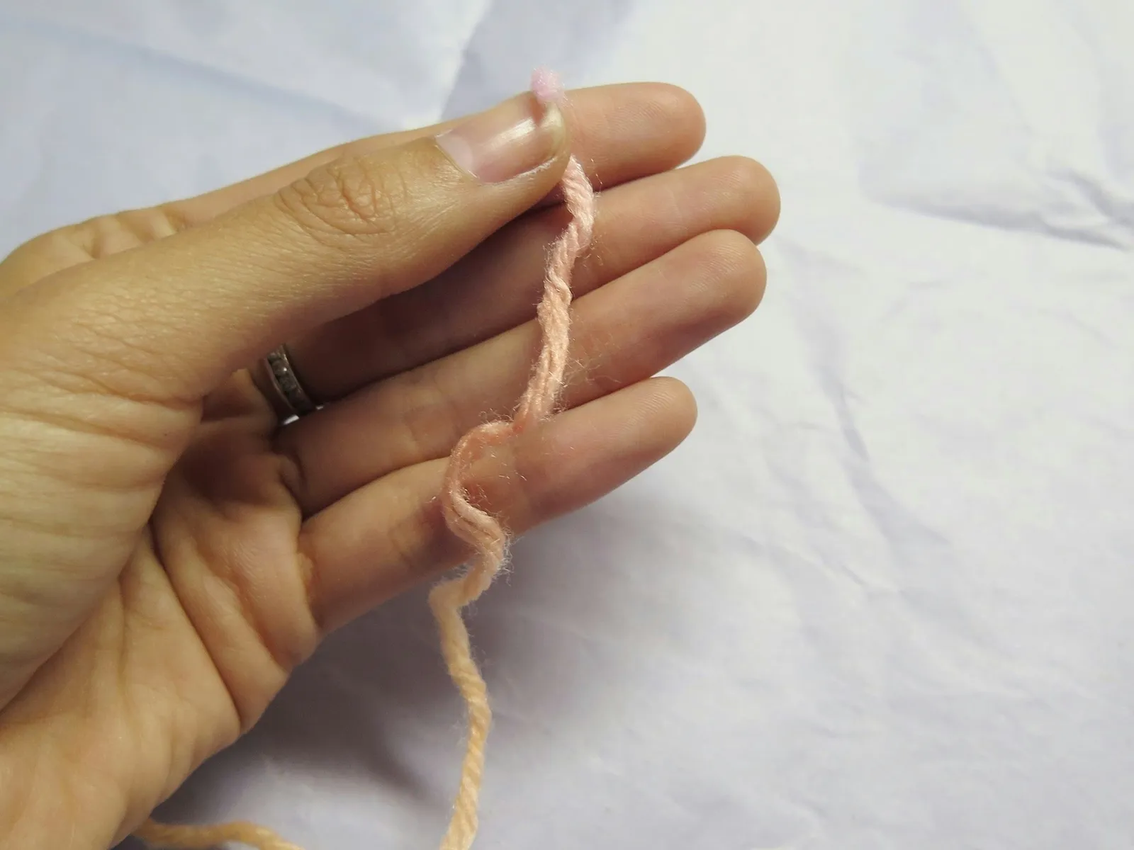 Hand holding a string of yarn, preparing to wrap the yarn around fingers